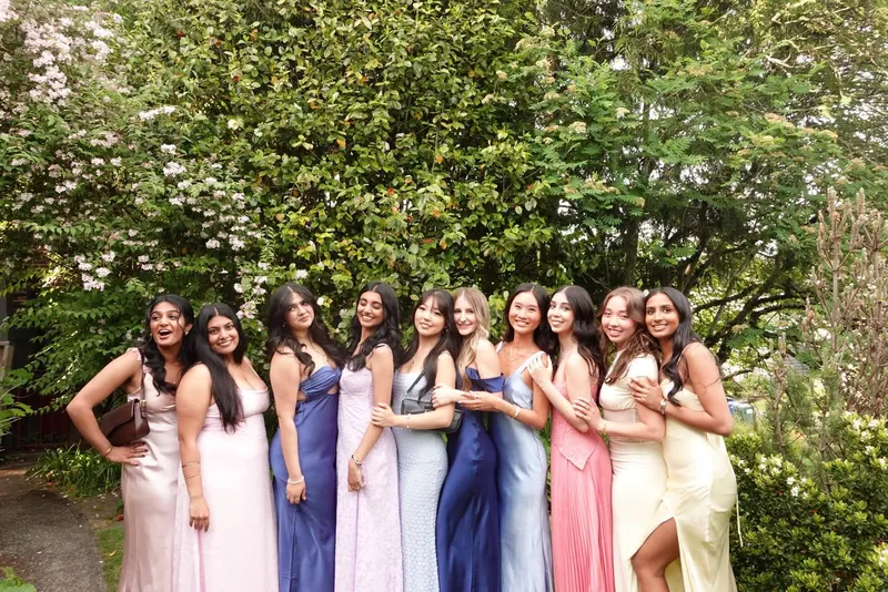 Brothers in formal dresses lined up in front of a flowering hedge
