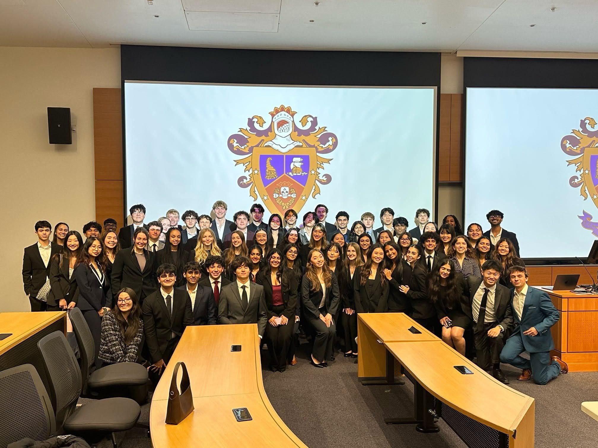 The whole chapter in business attire in a lecture hall, with the Delta Sigma Pi crest on the screen behind them